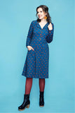 A woman wears a long-sleeved, blue Cissi och Selma dress Viveca Rävar midi shirt dress featuring a pattern of small orange foxes, paired with dark tights and black ankle boots.