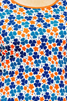 The Cissi och Selma Magda dress Klöver Orange by BUTIK KUBIK features a vibrant floral pattern with blue clovers and orange flowers on ekologisk bomullstrikå, inspired by 50-talets grafiska design.