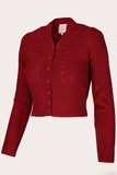 The Emmy - The Scandi Summer Cardi by BUTIK KUBIK in Lipstick Red is a vintage-inspired cropped knit cardigan with long sleeves, a V-neck, and button-down front. Made from merino wool, it features a cable-knit design with ribbed cuffs and hem for timeless appeal.