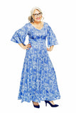 Smiling gray-haired woman with glasses wears the BUTIK KUBIK Cissi och Selma Greta klänning Sjögräs, featuring blue flared trumpet sleeves, and blue heels, standing confidently hands on hips against a white background.