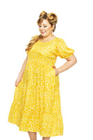 A woman with long blonde hair in vintage waves wears the Cissi och Selma Ida klänning Strandsten from BUTIK KUBIK. She smiles and looks down, standing against a white background.