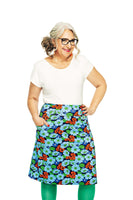 A confident, smiling woman with glasses and gray curly hair wears a white top and vibrant Cissi och Selma Majken Humlesurr blå skirt from BUTIK KUBIK, paired with green tights. Against a plain white background, she strikes a pose with one hand on her hip.