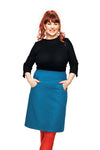A woman with long red hair smiles, wearing a black top, blue Cissi och Selma Majken kjol Jeans Petrol skirt by BUTIK KUBIK, red tights, and white earrings, standing with her hands in her skirt pockets against a white background.