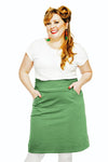 A smiling woman with long, wavy blonde hair wears a white shirt and the Cissi och Selma Majken skirt Jeans Salvia from BUTIK KUBIK, posing with hands in pockets against a plain white background.