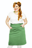 A smiling woman with long, wavy blonde hair wears a white shirt and the Cissi och Selma Majken skirt Jeans Salvia from BUTIK KUBIK, posing with hands in pockets against a plain white background.