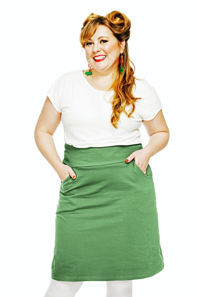 A smiling woman with long, wavy blonde hair wears a white shirt and the Cissi och Selma Majken skirt Jeans Salvia from BUTIK KUBIK, posing with hands in pockets against a plain white background.