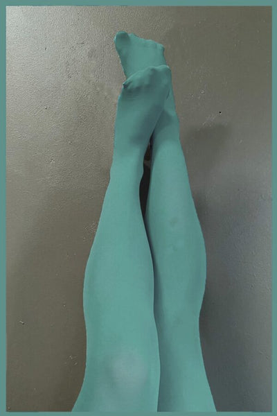A pair of legs in BUTIK KUBIK's Sneaky fox Blue Fusion nylonstrumpbyxor cross and stretch upward against a plain gray wall, framed by a matching teal border.