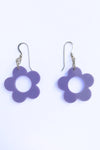 The Cissi & Selma Örhängen Frö Lavendel earrings by BUTIK KUBIK feature retro-inspired, lavender flower pendants with central holes, elegantly hanging from sterling silver hooks against a white backdrop.