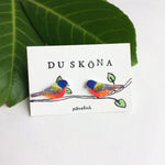 A small card showcases two colorful birds on a branch amid large green leaves. DU SKÖNA and påvefink embellish it, perfect for nature-inspired design lovers like BUTIK KUBIKs Du sköna bird earrings Påvefink.