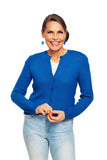A smiling woman wears the Cissi och Selma cardigan Sigrid Hav by BUTIK KUBIK over a white top and light blue jeans, standing against a white background with her hands clasped in front of her.