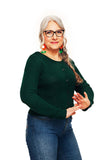 Older woman with long gray hair, glasses, and colorful earrings smiles while wearing the BUTIK KUBIK Cissi och Selma cardigan Sigrid Skog and jeans, standing against a plain white background with hands gesturing in front of her.