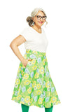 Smiling older woman with gray hair and glasses, wearing a white top and BUTIK KUBIK Cissi och Selma Solbritt skirt Humesurr lime, standing with one hand in her skirt pocket against a white background.