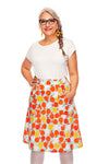 Smiling older woman with gray braided hair, glasses, and a white top wears the colorful Cissi och Selma Sonja skirt Äppelriket from BUTIK KUBIK with pockets, standing with one hand in her pocket against a white background.