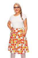Smiling older woman with gray braided hair, glasses, and a white top wears the colorful Cissi och Selma Sonja skirt Äppelriket from BUTIK KUBIK with pockets, standing with one hand in her pocket against a white background.