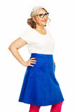 Smiling older woman with gray hair in a ponytail, glasses, white top, and bright pink tights wears a BUTIK KUBIK Cissi och Selma Sonja kjol Manchester Hav as she stands with one hand on her hip against a white background.
