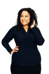 A woman with curly hair smiles while looking to the side, wearing a Cissi och Selma blus Susanne Marinblå from BUTIK KUBIK, posing with one hand on her hip and the other touching her hair against a white background.