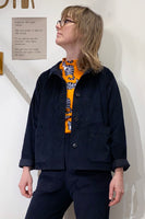 A person wearing glasses and the Kubik Overshirt black by BUTIK KUBIK stands in front of a white wall with a Swedish sign. Underneath, they wear a shirt with an orange background and abstract black-and-white patterns, enhancing the stylish oversized fit.