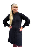 A woman with long blonde hair wears the Svea Kol dress by BUTIK KUBIK, featuring balloon sleeves, along with red earrings and mauve tights. She stands with hands on hips and smiles against a white background.