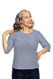 A smiling woman with gray hair wears the Cissi och Selma top Vendela Randig Blå by BUTIK KUBIK and white earrings, looking up with one hand in her hair against a white background.