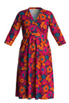 The Cissi och Selma dress Vera Humlesurr Magenta by BUTIK KUBIK is a V-neck long-sleeved dress in ekologisk bomull, featuring vibrant orange, pink, and blue floral patterns with a cinched waist for elegance.