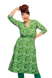 A woman poses playfully in a Cissi och Selma dress Vera Tigrar grön by BUTIK KUBIK, featuring a vibrant green zebra print and V-formed omlottringning. She pairs it with matching ekologisk bomullstrikå leggings, her expression cheerful against a plain white background.