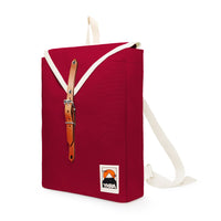 The YKRA Scout Bordeaux by BUTIK KUBIK is a practical small backpack, perfect for everyday use. Its made from red cotton canvas with a white strap and front flap, featuring a tan leather strap with buckle closure and a mountain logo patch with Ykra on the front bottom corner.