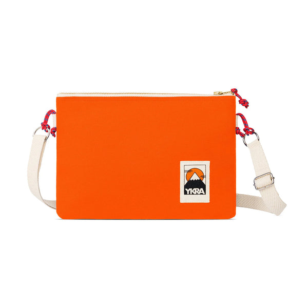 The YKRA Side Pouch Orange by BUTIK KUBIK is a rectangular crossbody bag with a white adjustable strap, red zipper cord, and a mountain Ykra logo patch—ideal as a travel pouch for your essentials.