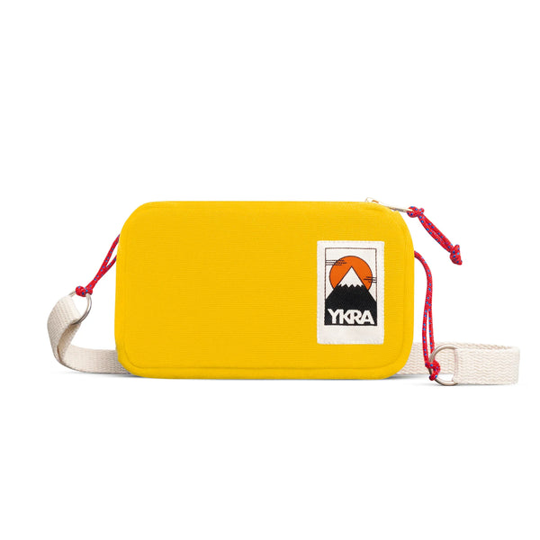 A compact yellow YKRA travel bag from BUTIK KUBIK, featuring a white adjustable strap, red cord accents, and a mountain-and-sun patch—perfect for staying organized on the go.