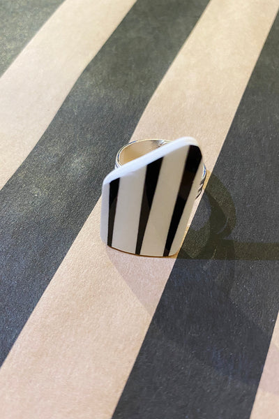 The Saved & remade ring porslin by BUTIK KUBIK features a silverplated band and a bold, angular face crafted from återbrukat porslin, blending seamlessly with the striped background for a striking visual effect.