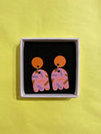 Törmi Nonparelli earrings pink by BUTIK KUBIK: Colorful Finnish birch plywood earrings with round orange tops, pink abstract shapes, and purple-orange patterns on yellow, presented in a white box with black interior.