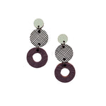The Törmi herkku earrings by BUTIK KUBIK are dangle earrings made from Finnish birch plywood, featuring three stacked circles: a small solid light circle, a medium black-and-white mesh circle, and a large textured dark purple open circle.